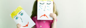 little girl holding up drawing of sad and happy faces
