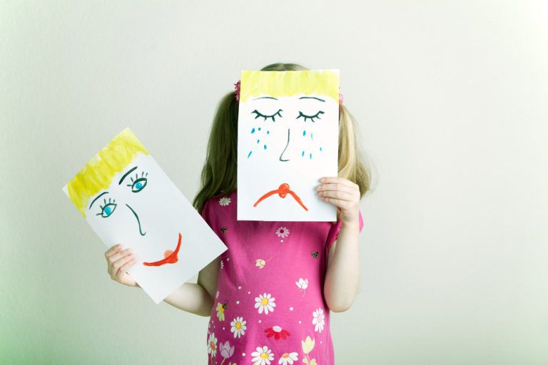 little girl holding up drawing of sad and happy faces