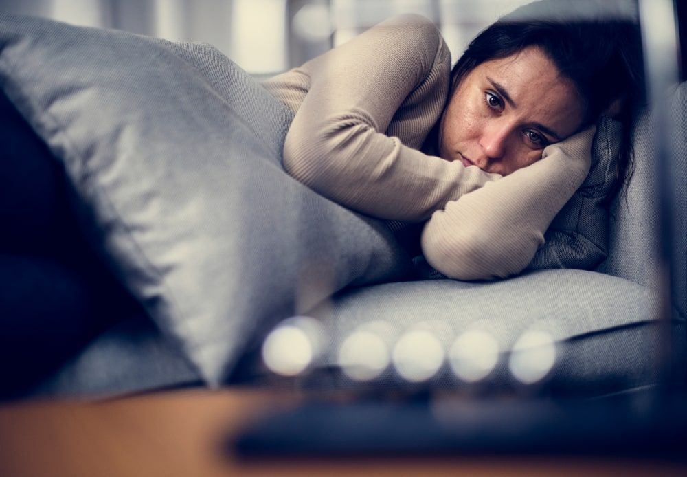 Woman lying on couch, snuggling a pillow and looking unhappy
