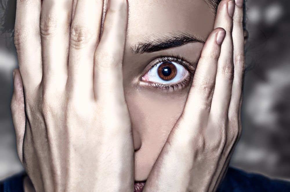 Woman holding both hands over her face, only peeking out with one terrified-looking eye