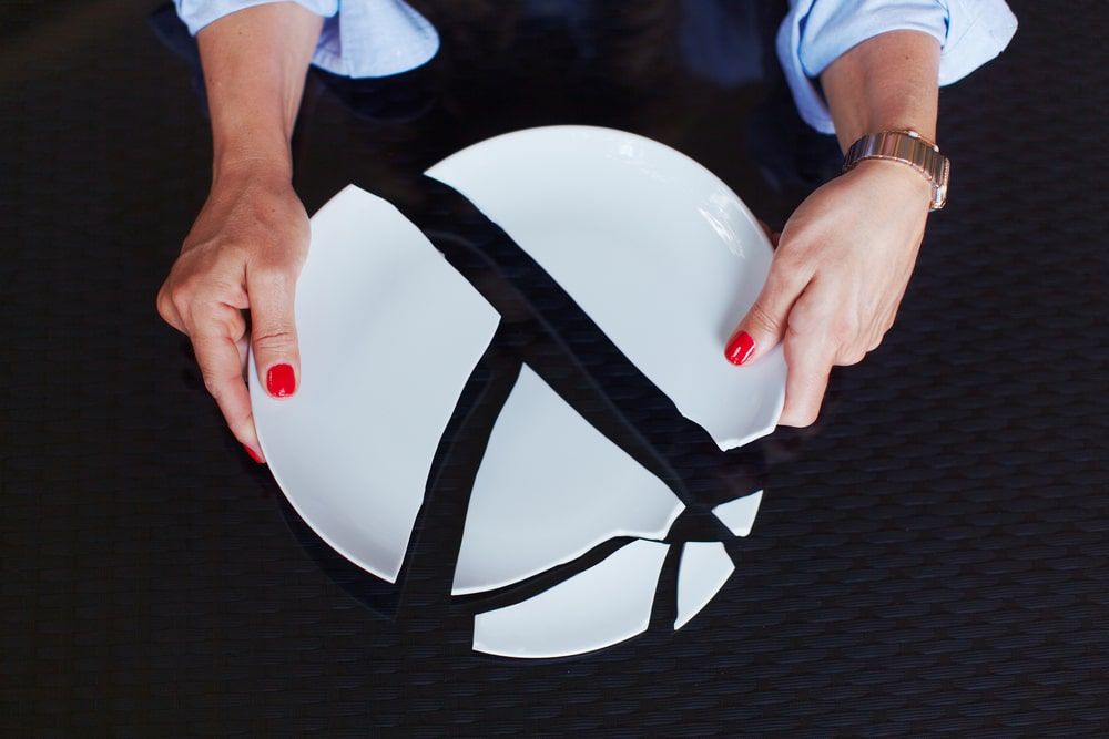 Woman holding pieces of a white broken plate against a black background