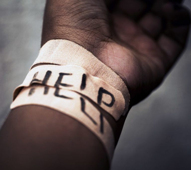Arm facing upwards with wrist bandaged and the word "help" scribbled across the bandages