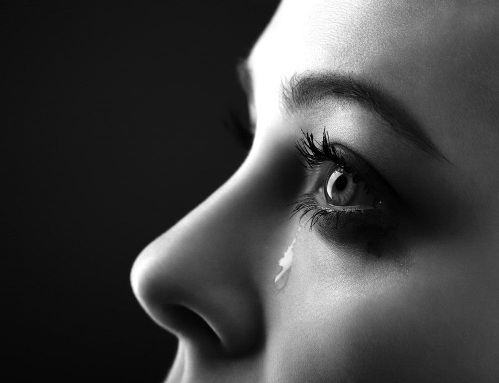 Black and white sideways closeup of a woman's eye and tear falling down her cheek