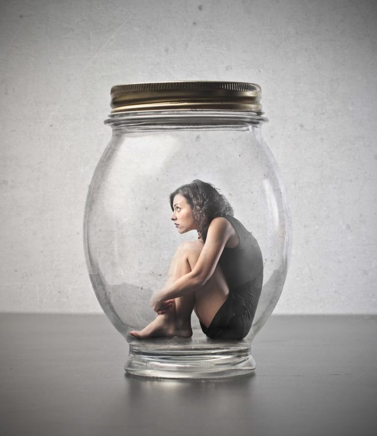 Woman sitting in the fetal position inside a giant glass jar