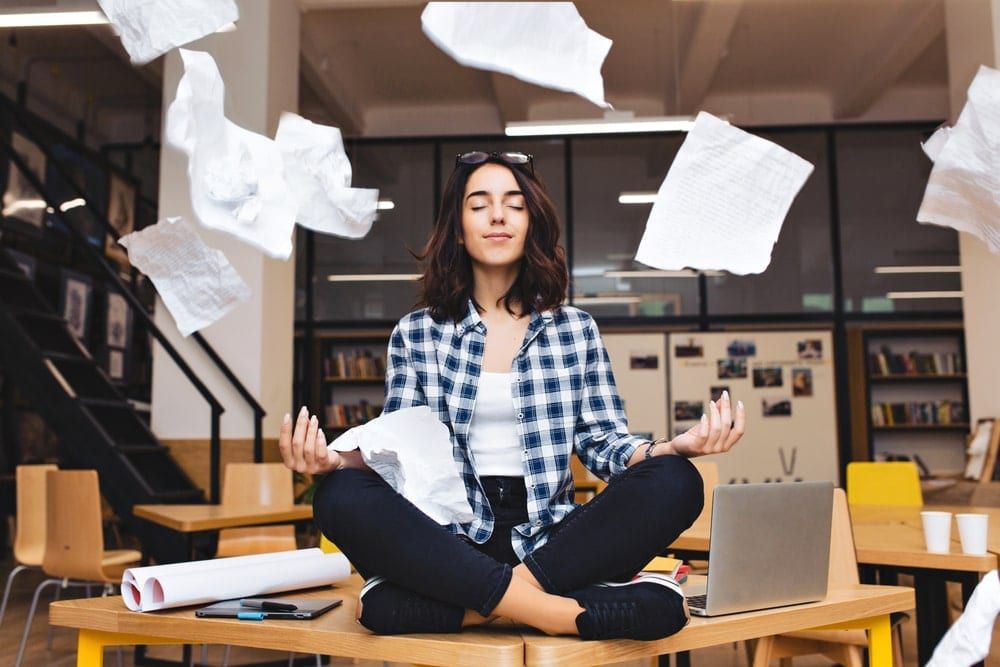 Woman meditating on her desk surrounded by work stress