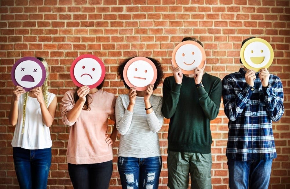 five people standing beside each other wearing masks of different emotions