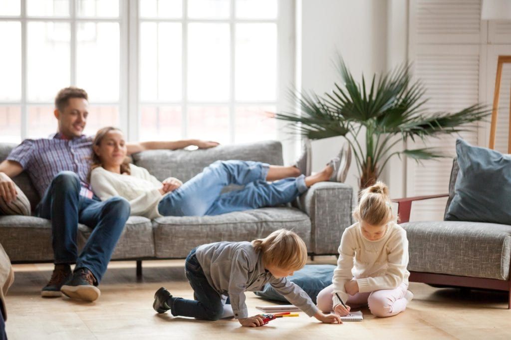Parents relaxing on the couch and watching their children play on the floor