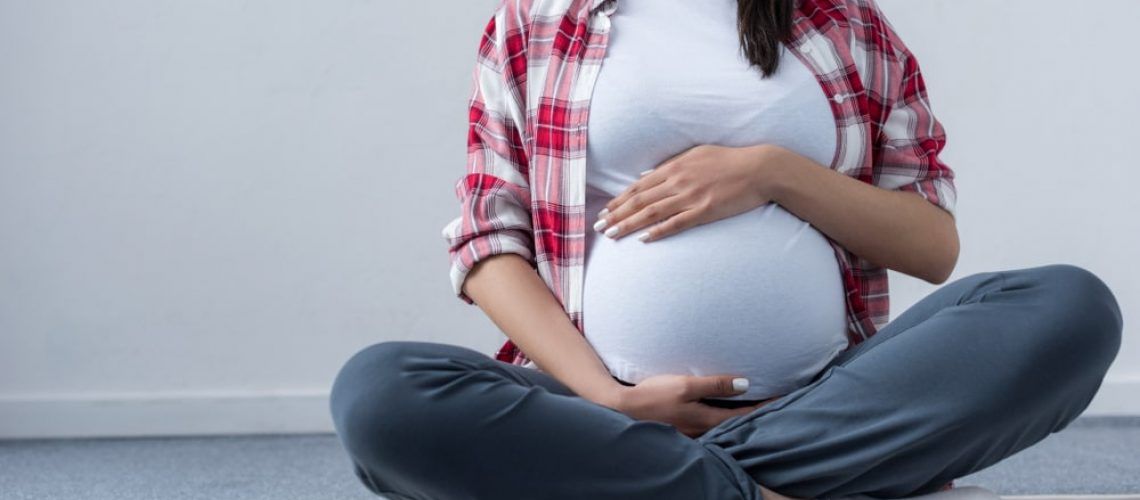 Lower half of pregnant woman sitting cross legged and holding her belly
