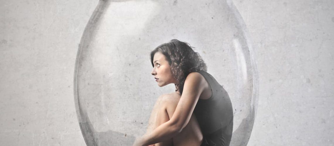 Woman sitting in the fetal position inside a giant glass jar